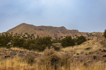 Small mountain range with cliff face behind yellow grass and brush in rural