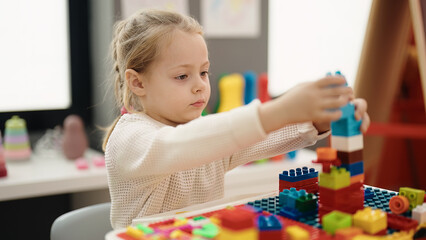 Adorable blonde girl playing with construction blocks sitting on table at kindergarten