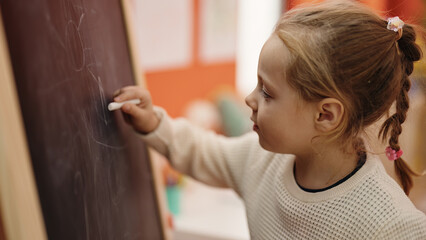 Adorable blonde girl preschool student drawing on blackboard at kindergarten