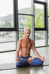 Obraz premium barefoot man in blue pants sitting in lotus pose and doing gyan mudra.