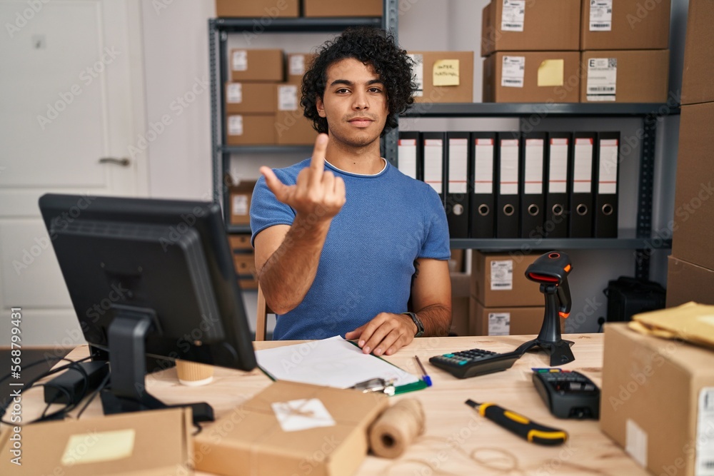 Canvas Prints Hispanic man with curly hair working at small business ecommerce showing middle finger, impolite and rude fuck off expression