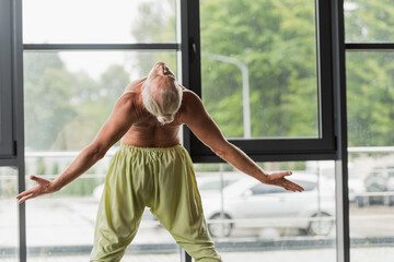 Fototapeta na wymiar shirtless man in green pants doing backside bend in yoga studio.