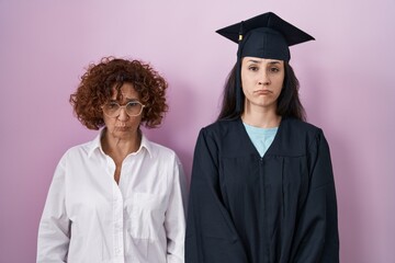 Hispanic mother and daughter wearing graduation cap and ceremony robe depressed and worry for...