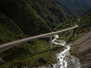 Cars driving on Otira Viaduct concrete bridge over green alpine valley river at Arthurs Pass...