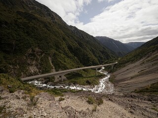 Cars driving on Otira Viaduct concrete bridge over green alpine valley river at Arthurs Pass...