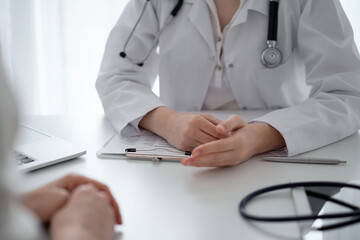 Doctor and patient discussing current health questions while sitting at the desk in clinic office, closeup. Medicine and healthcare concept
