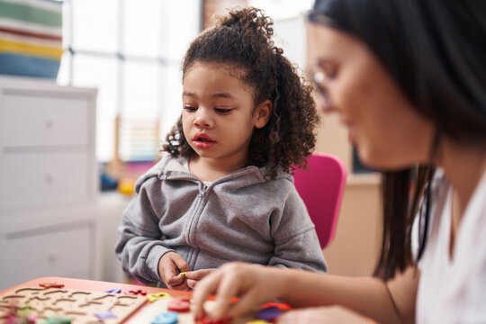 Teacher and toddler playing with maths puzzle game sitting on table at kindergarten