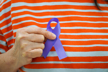 Elderly woman holding purple ribbon to help people living health care and world cancer day...