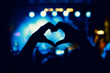 A person is making a heart sign during a concert of a favorite music band. Black silhouette.