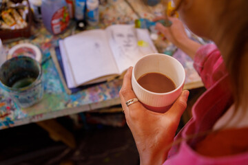 Female artists holding cup of tea while making sketch in background