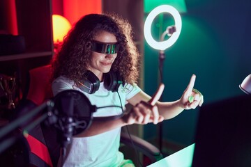 Young beautiful hispanic woman streamer playing video game using virtual reality glasses at gaming room