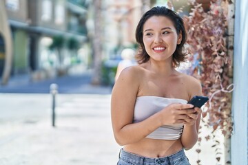 Young hispanic woman smiling confident using smartphone at street