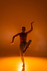 Fototapeta na wymiar full length of shirtless man in pants practicing yoga on orange background.