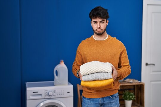 Hispanic man with beard holding clean folded laundry depressed and worry for distress, crying angry and afraid. sad expression.
