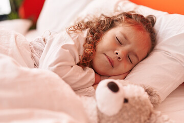 Adorable blonde toddler lying on bed sleeping with teddy bear at bedroom