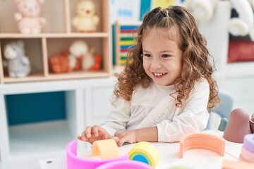Fototapeta premium Adorable blonde toddler playing with toys sitting on table at kindergarten