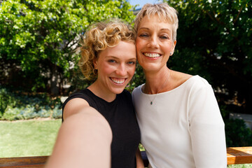 Fototapeta premium Portrait of smiling and embracing mother and daughter taking a selfie outdoors..