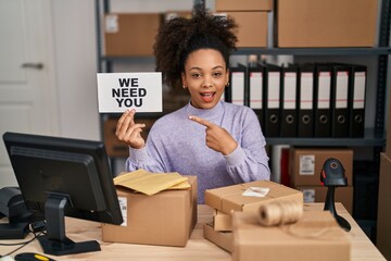 Fototapeta na wymiar Young african american woman working at small business ecommerce holding banner smiling happy pointing with hand and finger