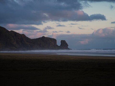 Idyllic black sand Te Henga Bethells beach with rock formation in background during sunset in West Auckland New Zealand