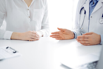 Doctor and patient discussing current health questions while sitting near of each other at the table in clinic, just hands closeup. Medicine concept