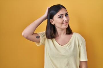 Hispanic girl wearing casual t shirt over yellow background confuse and wondering about question....