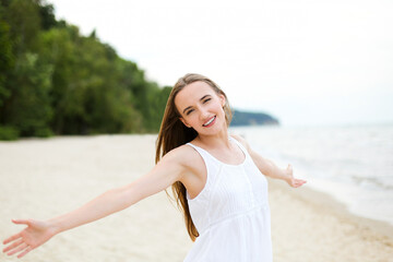 Fototapeta na wymiar Happy smiling woman in free happiness bliss on ocean beach standing with open hands. Portrait of a multicultural female model in white summer dress enjoying nature during travel holidays vacation 