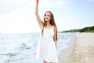 Fototapeta na wymiar Happy smiling woman in free happiness bliss on ocean beach catching clouds. Portrait of a multicultural female model in white summer dress enjoying nature during travel holidays vacation outdoors