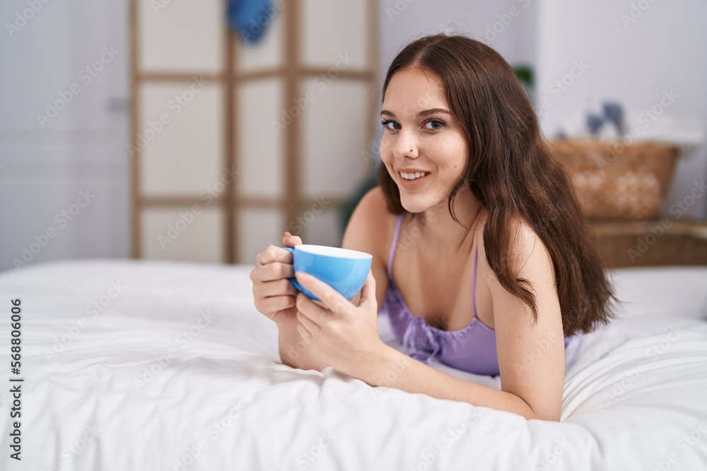 Poster Young woman drinking cup of coffee lying on bed at bedroom