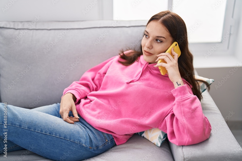 Wall mural young woman talking on the smartphone lying on sofa at home