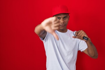 Young hispanic man singing song using microphone with angry face, negative sign showing dislike...