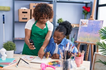 African american women teacher and student artist using smartphone drawing on notebook at art studio