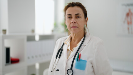 Middle age hispanic woman wearing doctor uniform standing with relaxed expression at clinic