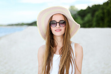 Portrait of a happy smiling woman in free happiness bliss on ocean beach standing with a hat and sunglasses. A female model in a white summer dress enjoying nature during travel holidays vacation 