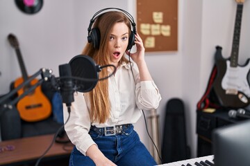 Young caucasian woman recording song at music studio scared and amazed with open mouth for surprise, disbelief face