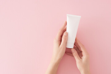 Skincare products concept. First person top view photo of female hands holding cosmetic bottle without label over pastel pink background with copy space. Beauty cosmetics mockup idea.