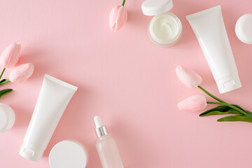 Nature skincare products concept. Flat lay photo of cosmetic tubes without label, serum bottles, cream jars and spring flowers on pastel pink background. Cosmetics spa mockup.