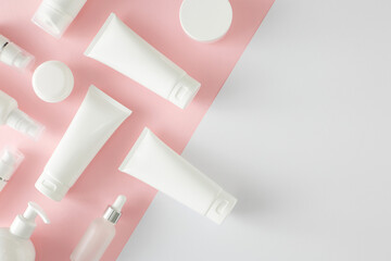 Skin care beauty concept. Top view composition made of cosmetic tubes, pump bottles, cream jars on pastel pink and white background with empty space. Flat lay cosmetics mockup idea.