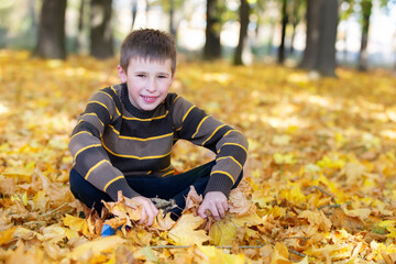 A teenage boy sits in an autumn park and looks into the camera.