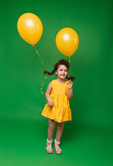 Funny little girl on a green background. A girl is having fun with yellow balloons. balloons lift up the pigtails of the child.