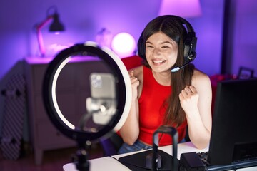 Young caucasian woman playing video games recording with smartphone screaming proud, celebrating victory and success very excited with raised arms
