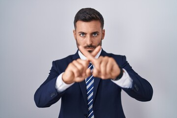 Handsome hispanic man wearing suit and tie rejection expression crossing fingers doing negative sign