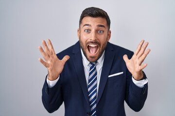 Handsome hispanic man wearing suit and tie celebrating crazy and amazed for success with arms raised and open eyes screaming excited. winner concept