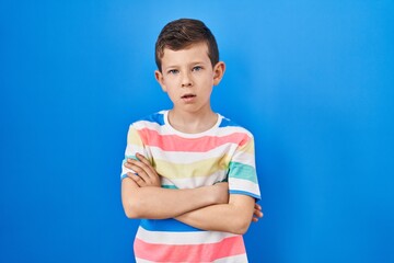 Young caucasian kid standing over blue background skeptic and nervous, disapproving expression on face with crossed arms. negative person.