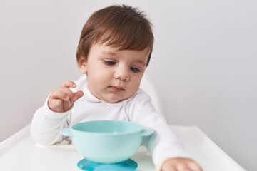 Adorable hispanic toddler sitting on highchair holding bowl over isolated white background