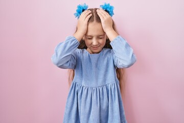 Young little girl standing over pink background suffering from headache desperate and stressed because pain and migraine. hands on head.