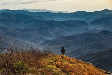 A young man with a backpack walks through the Caucasus Mountains on a sunny day. A tourist on a hike along the picturesque peaks at an altitude of 1000m.