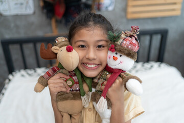 Sweet little girl is hugging a teddy bear, looking at camera and smiling while sitting on her bed at home