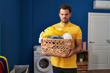 Young hispanic man holding laundry basket skeptic and nervous, frowning upset because of problem....