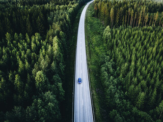 Aerial view of road with car through green woods in Finland.