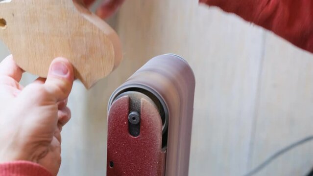 A professional carpenter processes a wooden billet with a belt grinder. Smooth movements